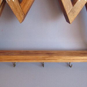 Puede incluir: Llavero de madera con forma de monta&ntilde;a con un estante y seis ganchos de metal. El marco es de madera marr&oacute;n claro con detalles blancos. El llavero est&aacute; montado en una pared gris.