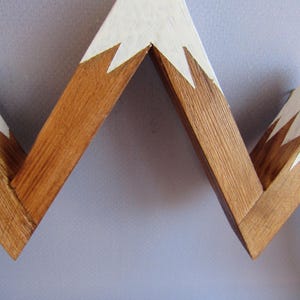 Puede incluir: Adorno de pared de madera con forma de cordillera. Las cimas est&aacute;n pintadas de blanco y la base es de color madera natural. El dise&ntilde;o es en zigzag, creando una silueta de monta&ntilde;a. Esta pieza decorativa es adecuada para un hogar r&uacute;stico o moderno.