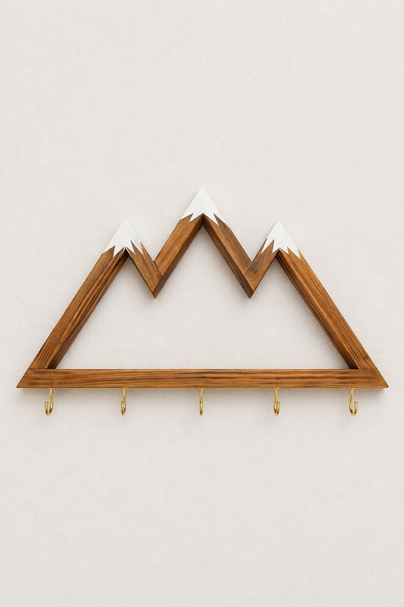 Puede incluir: Estanter&iacute;a de pared con forma de monta&ntilde;a de madera con acabado de madera natural y picos pintados de blanco. La estanter&iacute;a tiene cinco ganchos de color lat&oacute;n en la parte inferior, perfectos para colgar llaves o objetos peque&ntilde;os. Una pieza decorativa y funcional.