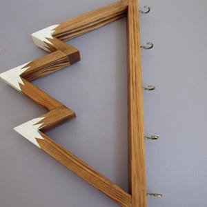 Puede incluir: Llavero de madera con dise&ntilde;o en zigzag y secci&oacute;n vertical con ganchos. La parte en zigzag est&aacute; te&ntilde;ida de marr&oacute;n con detalles blancos en las puntas. La secci&oacute;n vertical es de un tono de madera m&aacute;s claro y tiene varios ganchos met&aacute;licos.