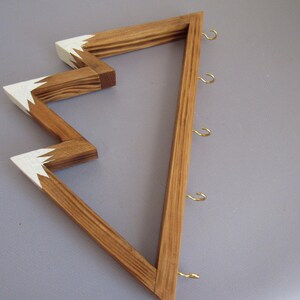 Puede incluir: Exhibidor de pared de madera con dise&ntilde;o en zigzag. La madera natural est&aacute; acentuada con pintura blanca en los puntos en zigzag. Cuenta con varios ganchos peque&ntilde;os de color dorado para colgar objetos. El exhibidor est&aacute; dise&ntilde;ado para montarse en la pared.