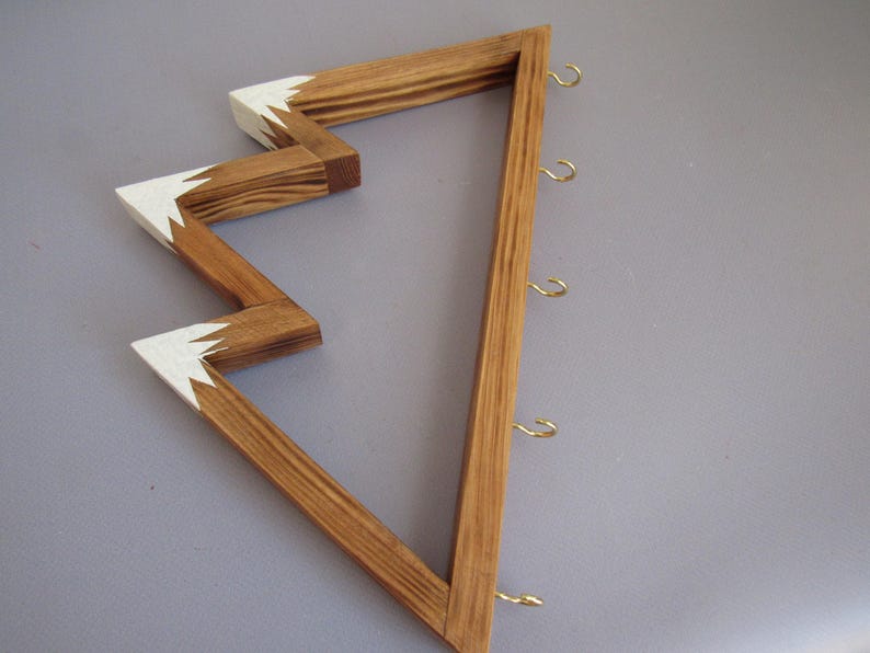 Puede incluir: Exhibidor de pared de madera con dise&ntilde;o en zigzag. La madera natural est&aacute; acentuada con pintura blanca en los puntos en zigzag. Cuenta con varios ganchos peque&ntilde;os de color dorado para colgar objetos. El exhibidor est&aacute; dise&ntilde;ado para montarse en la pared.