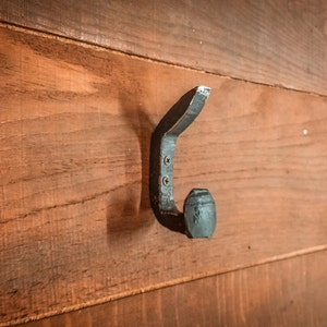 May include: A black metal hook with a rounded end, mounted on a wooden wall.