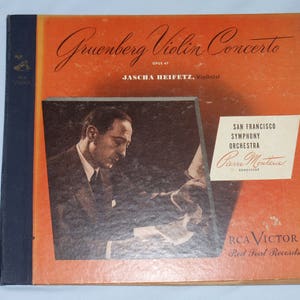 May include: A red and white vinyl record album cover featuring a black and white photo of violinist Jascha Heifetz performing the Gruenberg Violin Concerto, Opus 47, with the San Francisco Symphony Orchestra conducted by Pierre Monteux. The album is a Red Seal Records release by RCA Victor.