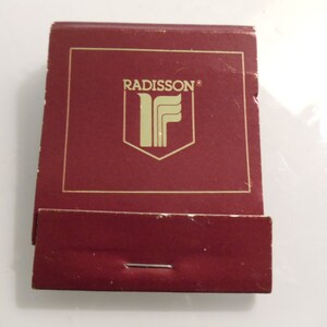 May include: A red matchbook with gold lettering that reads "RADISSON®" and a gold stylized "F" logo.