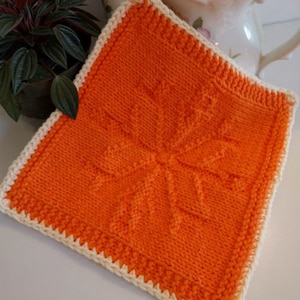 Op de afbeelding: Oranje en gele gebreide theedoek met een decoratief patroon.
