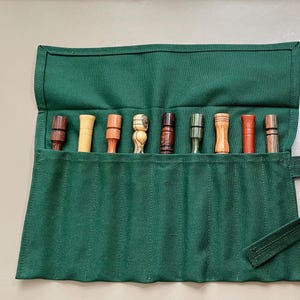 May include: A green canvas roll-up case with 10 slots for holding small tools or implements. The case has a strap and a separate green canvas pouch.