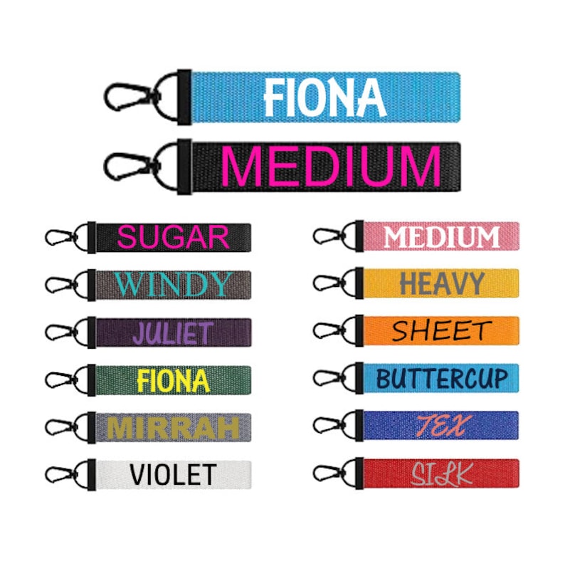May include: A collection of fabric keychains with various text in different colors. The keychains have a black clasp and a loop. The text includes names like "FIONA", "JULIET", and words like "MEDIUM" and "SILK".