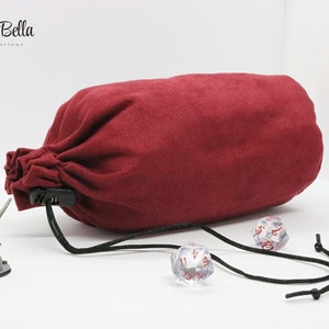 May include: A red velvet dice bag with a black drawstring and a plastic clasp. The bag is lying on a white surface with a miniature figure and dice nearby.