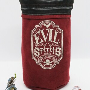 May include: A red velvet dice bag with a black drawstring top. The bag has an embroidered design that says "Evil Spirits Est. 1776" with a skull and crossbones below the text.