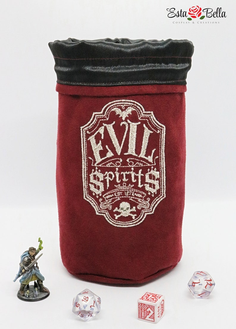 May include: A red velvet dice bag with a black drawstring top. The bag has an embroidered design that says "Evil Spirits Est. 1776" with a skull and crossbones below the text.