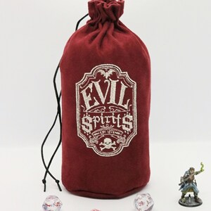 May include: A red velvet dice bag with a white embroidered design that says "Evil Spirits" with a skull and crossbones. The bag is tied with a black drawstring and is sitting on a white surface with dice and a miniature figure.