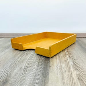 Peut inclure: Un plateau de bureau en bois jaune clair de forme rectangulaire. Le plateau a un profil bas avec un bord avant légèrement incurvé et un bord arrière surélevé. Le grain du bois est visible et le plateau semble en bon état.