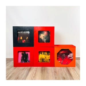 Op de afbeelding: Een verzameling vierkante houten opbergkubussen in rood, zwart en oranje. Elke kubus toont albumhoezen. De linkerbovenkubus is zwart en heeft de tekst "mon drop". De andere kubussen zijn rood en oranje, met verschillende albumhoezen.