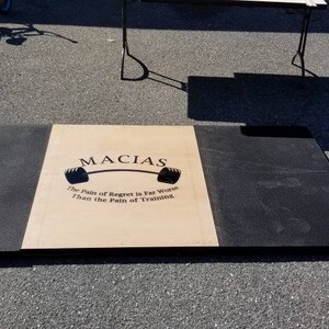May include: A black and beige weightlifting platform with the words "MACIAS" and "The Pain of Regret is Far Worse Than the Pain of Training" printed on the beige section.