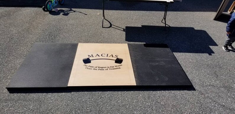 May include: A black and beige weightlifting platform with the words "MACIAS" and "The Pain of Regret is Far Worse Than the Pain of Training" printed on the beige section.