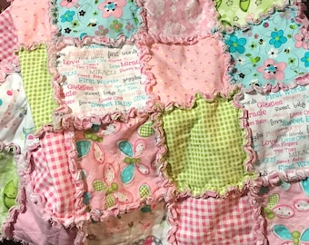 Puede incluir: Una colcha de bebé de retazos rosa, verde y blanca con un borde rizado. La colcha está hecha de varias telas con diferentes patrones, incluyendo flores, mariposas y cuadros.