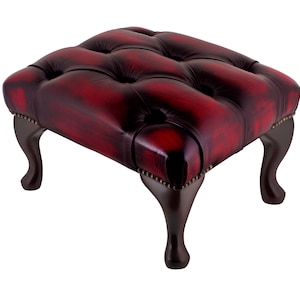 May include: A red leather footstool with a tufted top and four wooden legs.
