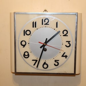 May include: A white square clock with black numbers and hands. The clock has a silver face and is mounted on a wall.