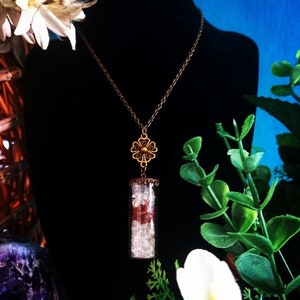 May include: A gold chain necklace with a flower pendant and a glass vial filled with white and red crystals.