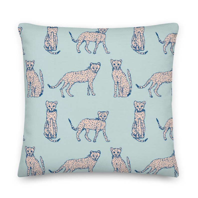 May include: A light blue throw pillow with a repeating pattern of cheetah print animals in a light pink color. The cheetah print is outlined in dark blue.