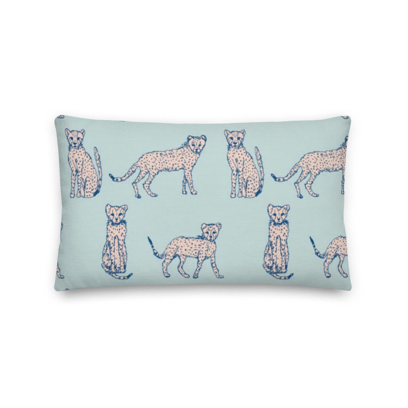 May include: A light blue throw pillow with a repeating pattern of pink cheetahs with blue spots. The cheetahs are in various poses, including sitting, standing, and running.