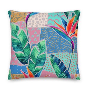 May include: A colorful throw pillow with a tropical print featuring green banana leaves, orange and blue bird of paradise flowers, and a patchwork background of pink, blue, and yellow geometric shapes.