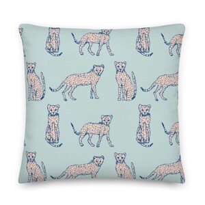 May include: A light blue throw pillow with a repeating pattern of cheetah print animals in a light pink color. The cheetah print is outlined in dark blue.