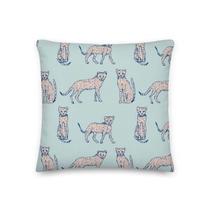 May include: A light blue throw pillow with a repeating pattern of pink and blue cheetahs. The cheetahs are in various poses, including sitting, standing, and running.