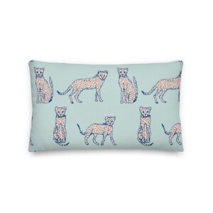 May include: A light blue throw pillow with a repeating pattern of pink cheetahs with blue spots. The cheetahs are in various poses, including sitting, standing, and running.