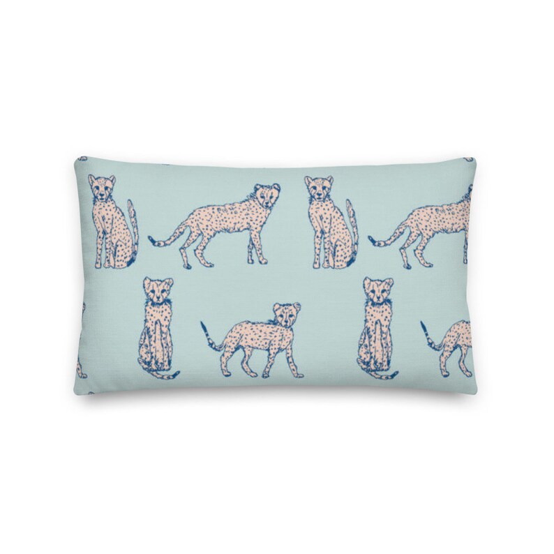 May include: A light blue throw pillow with a repeating pattern of pink cheetahs with blue spots. The cheetahs are in various poses, including sitting, standing, and running.