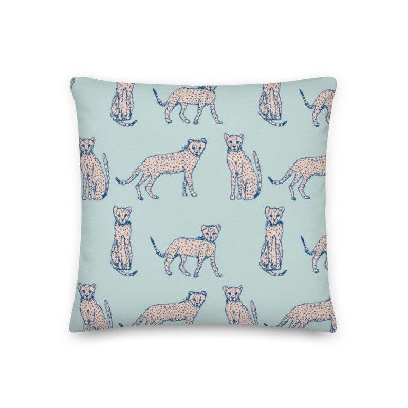 May include: A light blue throw pillow with a repeating pattern of pink and blue cheetahs. The cheetahs are in various poses, including sitting, standing, and running.