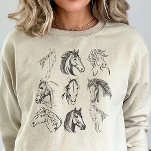 May include: A beige sweatshirt with a graphic print of nine horse heads in black. The horse heads are arranged in a grid pattern.