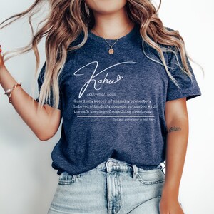 May include: Navy blue t-shirt with the word "Kahu" in a cursive font, along with a definition. The definition describes a guardian, keeper of animals, and protector. The shirt is a crew neck and is made of a soft material.