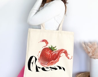 Puede incluir: Una bolsa de tela blanca con un gráfico de fresa roja y salpicaduras de jugo rosa. El texto "Fresh" está impreso en negro debajo de la fresa.