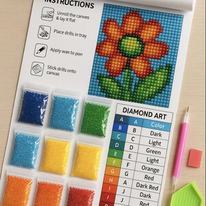 May include: Diamond art kit with a colorful flower design. Includes a canvas, bags of colored drills, a pink pen, a green tray, and an eraser. Instructions are printed on the top of the canvas.