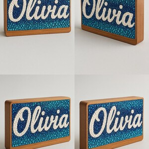 May include: Wooden nameplate with the name "Olivia" in white script. The name is set against a textured blue background, framed by a light brown wooden border. The nameplate is rectangular and appears to be a decorative item.