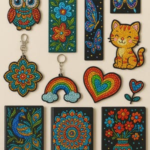 May include: A collection of colorful, beaded art pieces including keychains, bookmarks, and small notebooks. Designs feature an owl, peacock, rainbow, butterflies, flowers, a cat, a heart, and a mandala, all with intricate dot patterns.