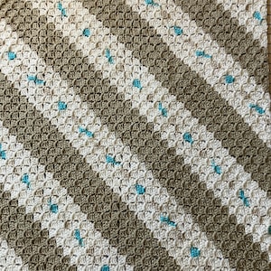 Könnte beinhalten: Eine gehäkelte Decke mit einem diagonalen Muster in Beige und Weiß mit blauen Akzenten.