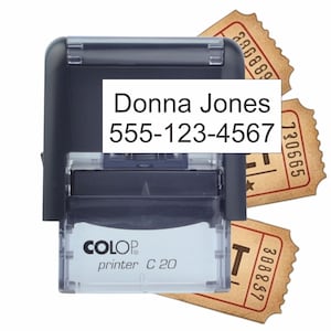 May include: A black Colop Printer C 20 self-inking stamp featuring the text Donna Jones 555-123-4567 on a white rectangular label. Behind the stamp are three tan-colored vintage-style paper tickets with scalloped edges and black serial numbers.