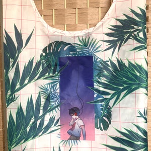 May include: A white reusable shopping bag with a pink grid pattern and a tropical leaf design. The bag features a graphic of a person wearing headphones and standing in front of a purple and pink gradient background.