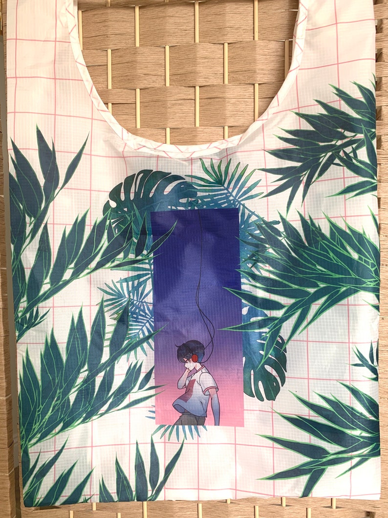 May include: A white reusable shopping bag with a pink grid pattern and a tropical leaf design. The bag features a graphic of a person wearing headphones and standing in front of a purple and pink gradient background.