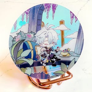 May include: A round, iridescent acrylic display featuring a colorful anime-style illustration. The artwork depicts a character in a fantasy setting with a blue sky, clouds, and floral elements. The display is held by a copper-colored metal stand.