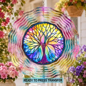 May include: A circular wind spinner featuring a central tree of life design with a vibrant rainbow gradient background. The outer edge has a wavy, metallic, iridescent finish that reflects light. The text READY TO PRESS TRANSFER is visible.