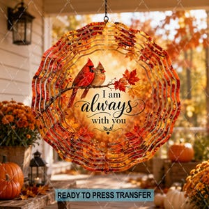 May include: A circular metal wind spinner featuring a printed design of two cardinals perched on a branch surrounded by autumn leaves. The text "I am always with you" is centered in black script. The edges are scalloped with a wavy pattern.