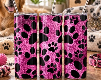 May include: Three cylindrical tumblers with a vibrant pink glitter finish and a repeating black paw print pattern. Each tumbler features a clear lid and a straight silver metal straw inserted into the top. The design is consistent across all three.