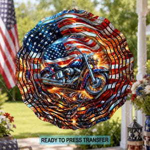 May include: A circular metal wind spinner featuring a graphic of a motorcycle against a backdrop of the American flag and orange flames. The design incorporates red, white, and blue colors with a metallic finish and a scalloped, layered edge.