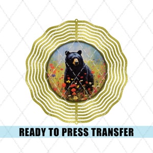 May include: A black bear stands in a field of wildflowers. The bear is surrounded by a gold metal wind spinner with a circular design. The wind spinner is ready to press transfer.