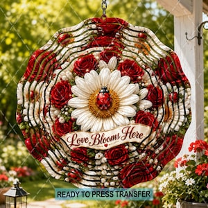May include: A circular wind spinner featuring a vibrant floral design with red roses and white daisies. A ladybug rests on the central daisy. A cream-colored banner across the center displays the text Love Blooms Here in brown script.