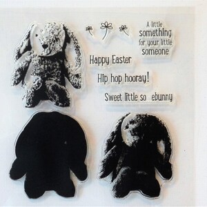 May include: A set of four clear rubber stamps featuring a bunny rabbit design. The stamps include a bunny rabbit with a textured surface, a bunny rabbit outline, and two text stamps that read "Happy Easter" and "Hip hop hooray! Sweet little so ebunny".